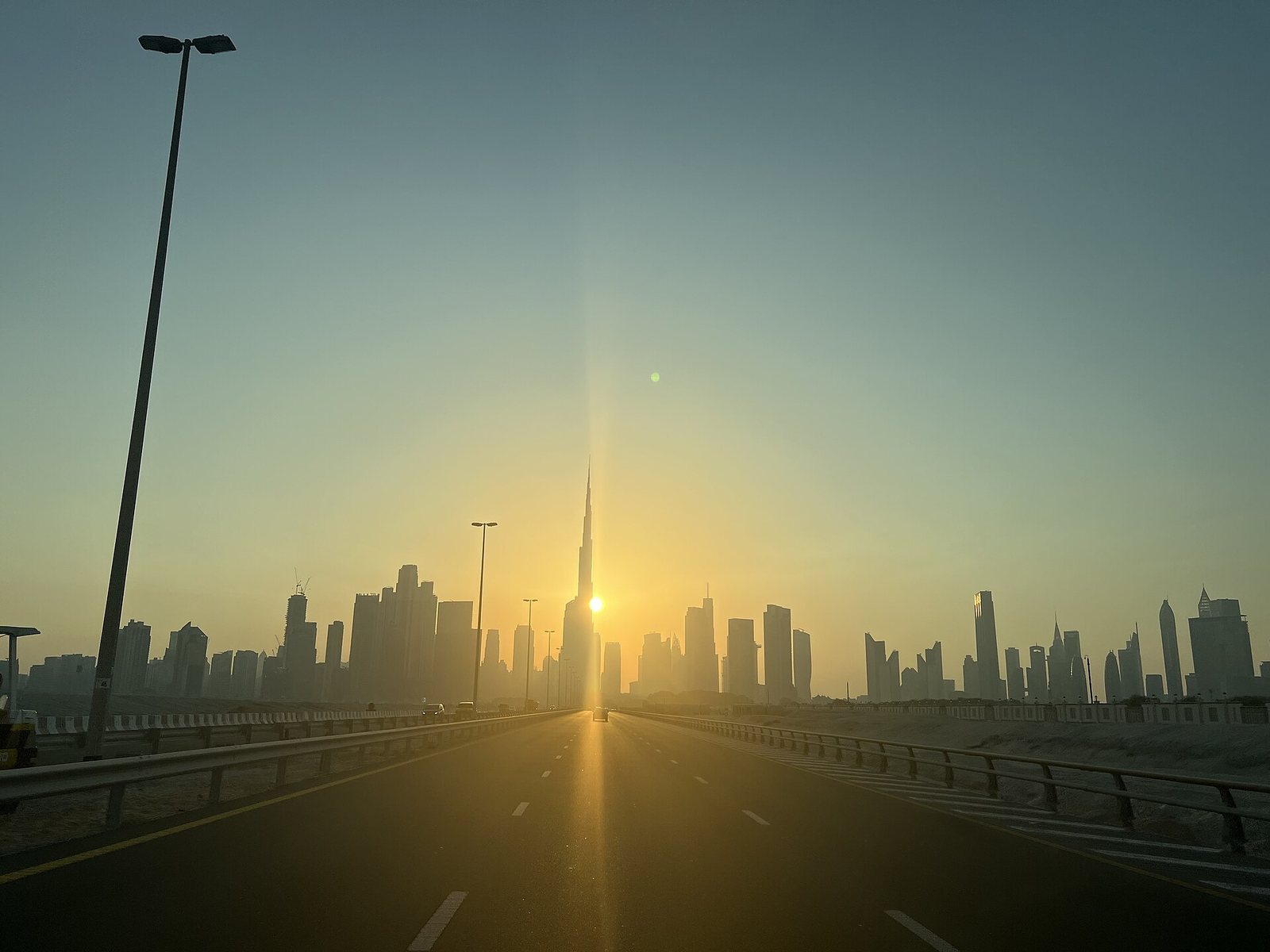 Downtown Dubai and the Burj Khalifa against the setting sun, seen down an empty highway
